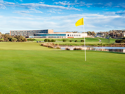 Yellow flagpole on the RACV Torquay golf course, in front of greenery and the resort.