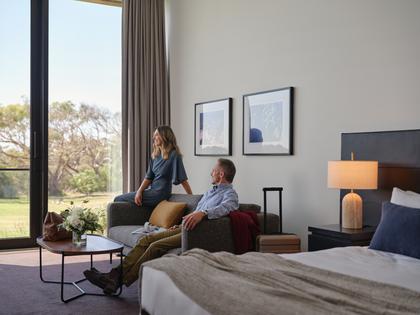 Couple relaxing in Golf View Room at RACV Torquay Resort, featuring a king bed, couches and desk.