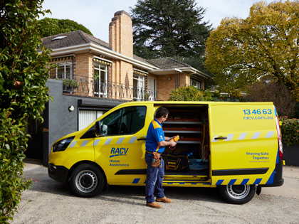 Tradesman standing in front of a yellow RACV van parked in driveway with its sliding door open.