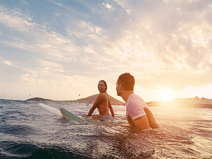 Two surfers sitting on their boards in the ocean at sunset.