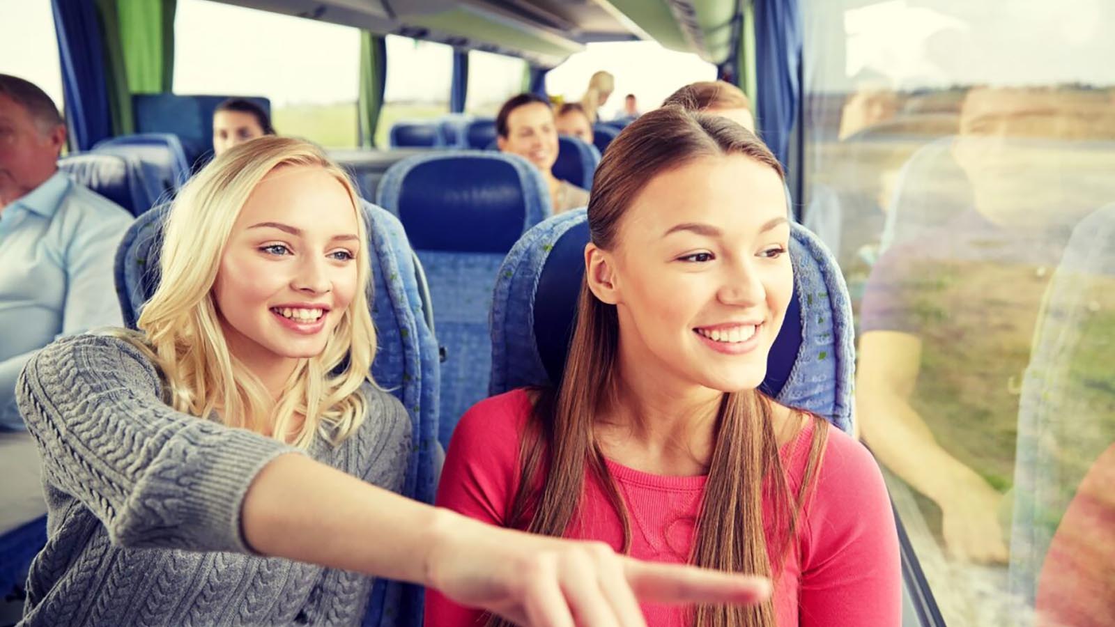 Two women riding on a bus, one pointing to look out the window.