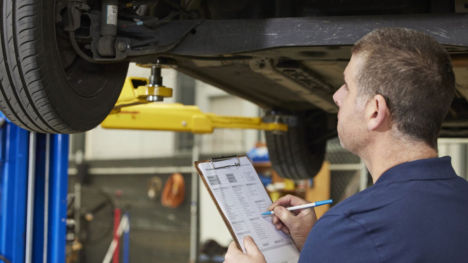 A mechanic witha clipboard assessing a vehicle.